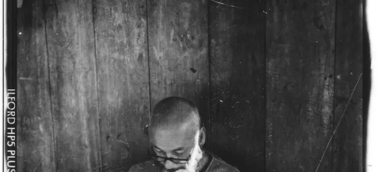 Foto en blanco y negro, tomada con cámara análoga, de una persona mirando hacia abajo frente a un fondo de madera